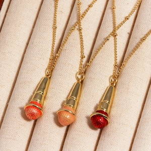 Three gold hip hop microphone pendants with orange peach and red heads on ribbed fabric