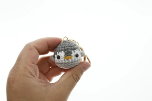 Handmade crochet penguin keychain with grey and white wool details and golden ring