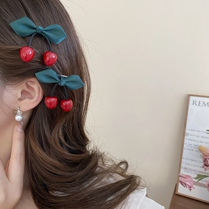 Close-up of red resin cherry hair clip with dark green bow on brown hair