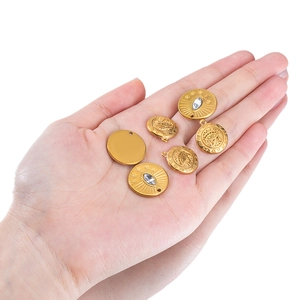 Golden stainless steel round eye charms with zircon inlays held in hand for size scale