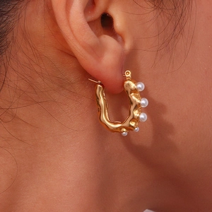 Detailed close-up of a U-shaped gold earring with irregular waves and five white pearls