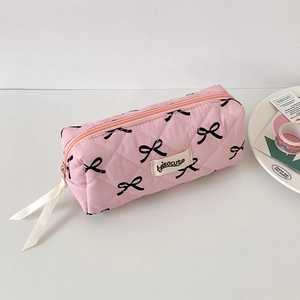 Detail of pink quilted pencil case with bow prints and brand label on white desk