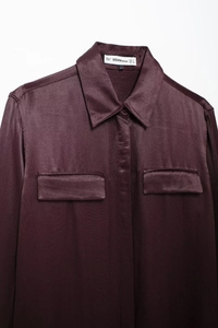 Detailed view of burgundy satin shirt collar and button pockets with smooth texture