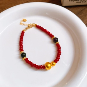 Détail macro du bracelet à perles rouges avec breloque Wu Lou dorée sur plateau