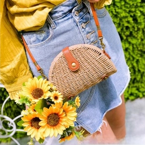 Detail of a semi-circular woven straw crossbody bag with brown leather flap and metal buckle