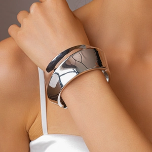 Close-up of a wide polished silver metal cuff bracelet featuring irregular wavy contours