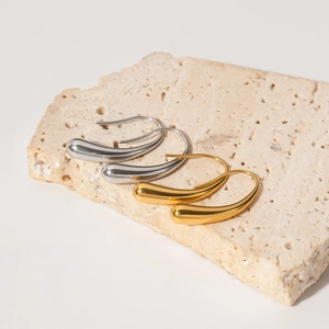 Polished gold and silver teardrop earrings displayed on a textured stone surface