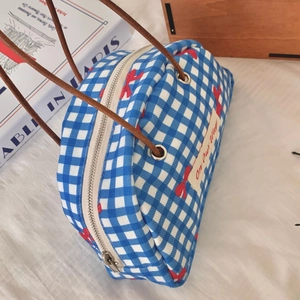 Close-up of blue plaid canvas handbag with red bow pattern and brown leather straps