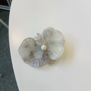 Macro detail of orchid hair clip with iridescent petals and a central pearl accent