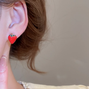 Close-up of model wearing a red strawberry stud earring with green leaf detail