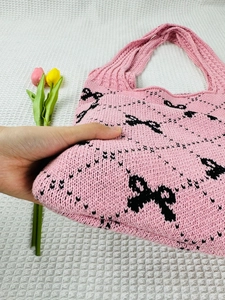 Detailed close-up of pink knitted tote bag featuring a black bow pattern and soft texture