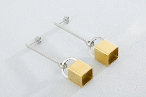 Detail of silver long bar earrings with gold hollow cube pendants in minimalist style