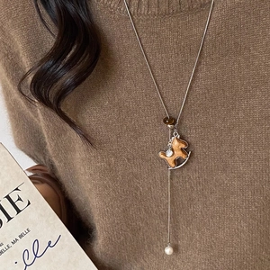 Detail of Trojan horse pendant necklace with white pearl on a brown sweater background