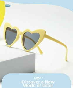 Detail view of heart-shaped yellow sunglasses for kids with grey lenses on a white stand