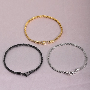 Detail view of woven rope chains in gold, black, and silver finishes on textured fabric