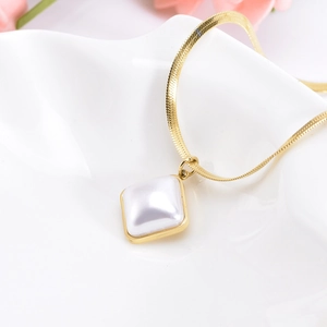 Detailed shot of golden snake chain necklace with square pendant on white ceramic plate