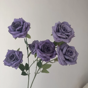Close-up of five realistic purple silk roses with green leaves and a small flower bud