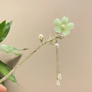 Nahaufnahme einer blassgrünen Blumenhaarnadel mit goldenem Zweig und Perlenquasten