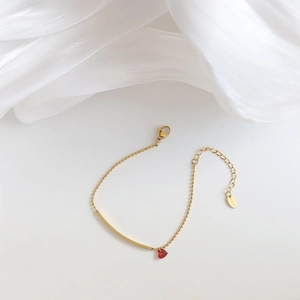 Detail of gold-plated stainless steel bracelet with curved tube and red heart charm