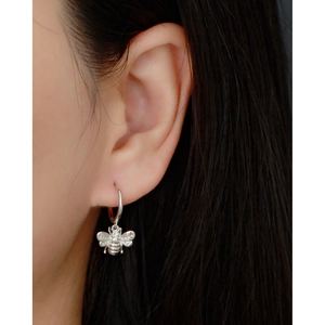 Detailed view of an S925 sterling silver bee pendant earring on a female ear