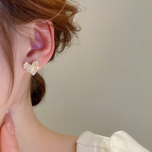 Close-up of heart-shaped crystal stud earrings in gold finish on ear model