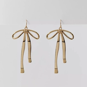 Elegant gold ribbon bow earrings with a polished metallic finish on a plain background