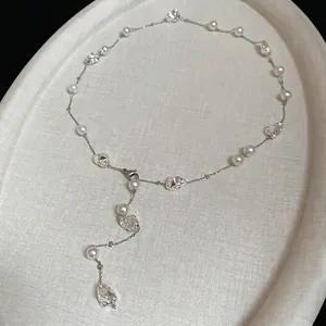 Elegante collana a Y argentata con perle irregolari e pendenti metallici su un vassoio