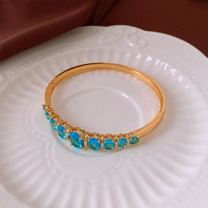 Détail d'un bracelet jonc doré avec gemmes bleu ciel sur une assiette en porcelaine