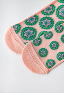 Detail of sheer pink mesh socks featuring green and pink snowflake embroidery patterns
