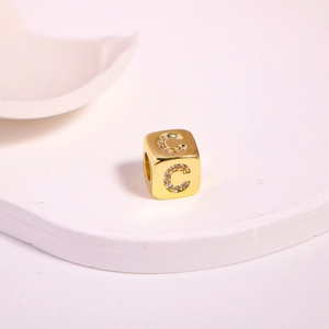 Detailed macro view of a gold cube bead featuring a sparkling cubic zirconia letter C inlay