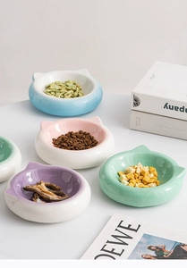 Four cat-ear shaped ceramic pet bowls in pastel colors shown on a minimalist white surface