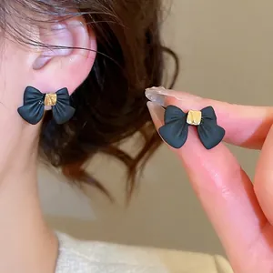 Elegant matte black bow earrings with gold square accents shown on a model