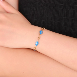 Detail of gold beaded Hamsa Hand bracelet with blue evil eye enamel on a female wrist