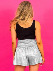 Back view of high waisted metallic silver shorts and black tank top on a pink background