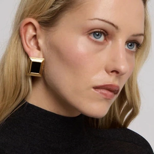 Macro shot of gold square stud earrings with black inlay worn on a model's ear