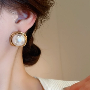 Close-up of a large round pearl earring with gold wire woven detail on model ear