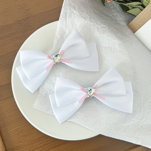 Détail de barrettes à double nœud en satin blanc avec centre rose et cristal en cœur