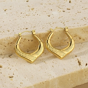Detailed macro view of V-shaped gold hoop earrings with textured grid patterns on stone