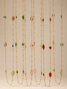 Detail von langen Goldketten mit bunten Marquise-Kristallanhängern und Perlen