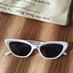 Close-up of white cat-eye children's sunglasses with dark lenses on a wood surface