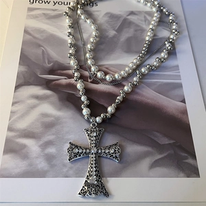 Detailed view of layered pearl and bead necklace with a large rhinestone cross pendant