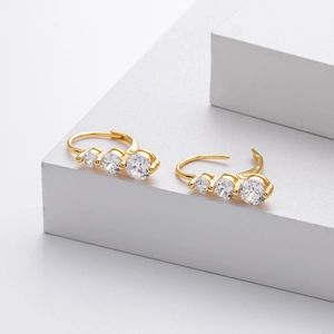 Détail de boucles d'oreilles dorées avec trois zircons blancs sur support blanc