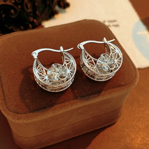 Macro shot of silver hollow flower hoop earrings on a luxury brown velvet jewelry box