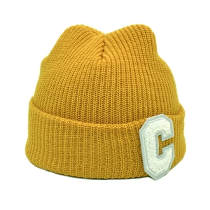 Détail d'un bonnet en maille côtelée jaune avec un écusson lettre C blanc