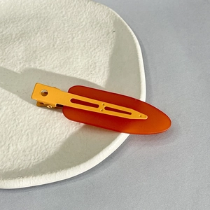Detail of red and orange matte hair clips placed on a white ceramic plate edge