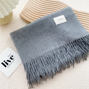 Detail of grey fringe scarf with soft knit texture and woven label for winter warmth
