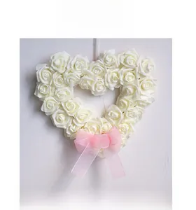 Vue frontale d'une couronne de roses blanches en cœur avec nœud rose de mariage