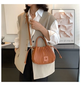 Detail of vertical pleated brown bucket bag featuring square buckle and leather handle