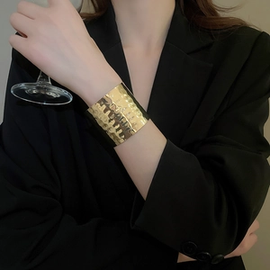 Close-up of golden wide cuff bracelet with hammered texture and minimalist metal finish