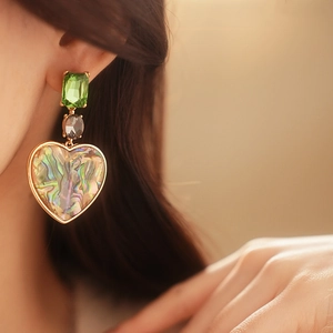 Close-up of vintage heart drop earring with green crystal and abalone shell on ear